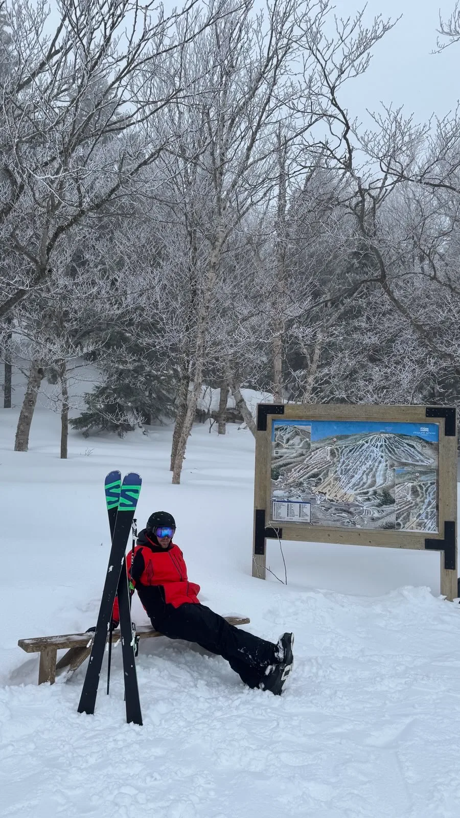 A skier resting by the Mount Snow trail map after a run