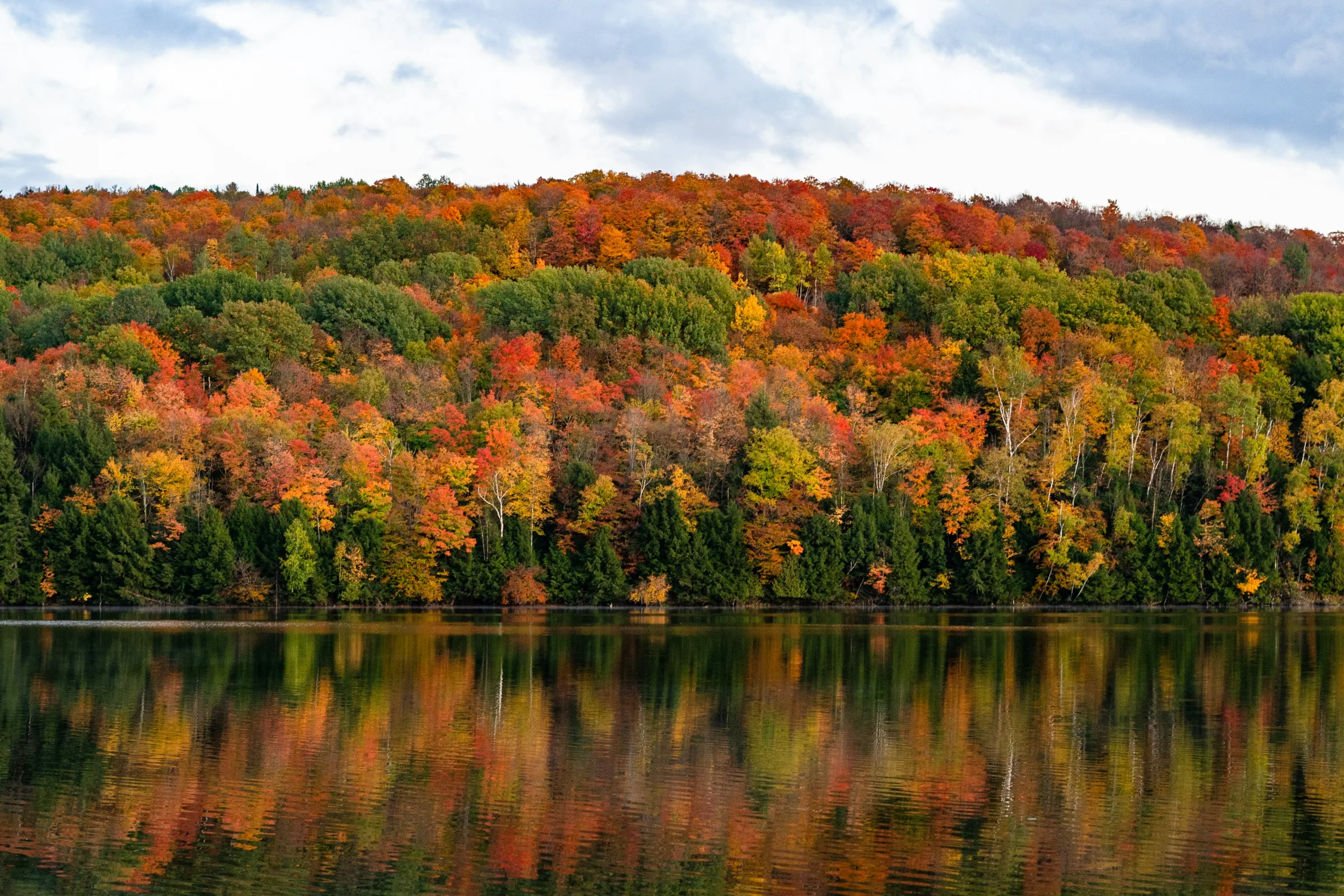 A foliage hillside reflected in a still Vermont lake