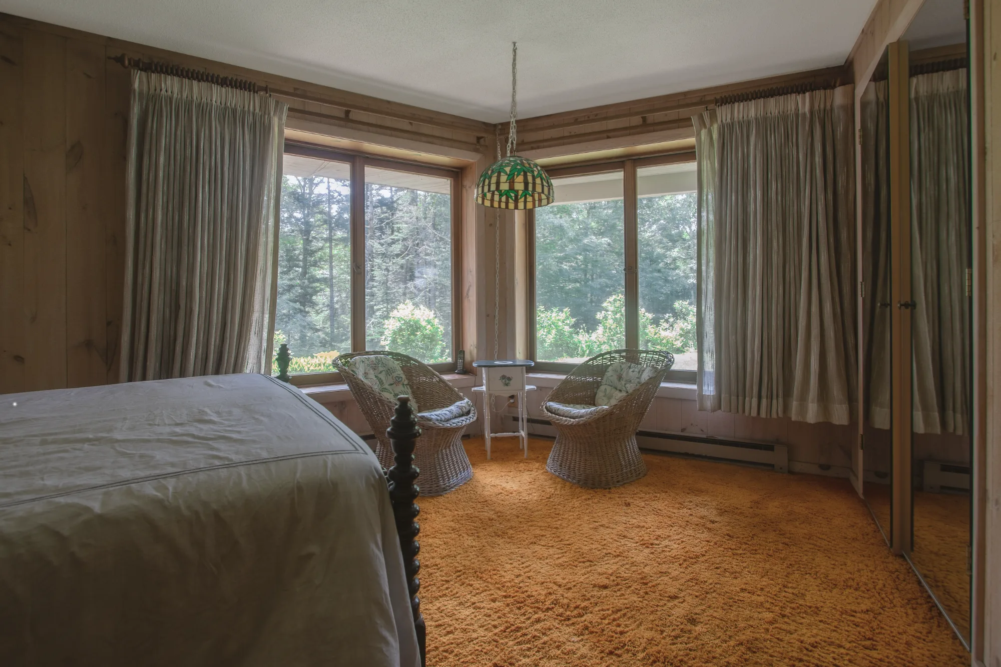 A bedroom with wicker chairs and forest views through corner windows