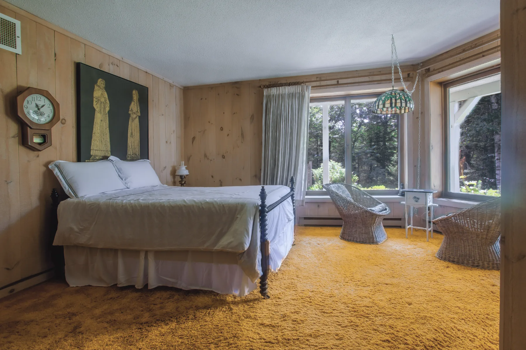 A pine-panelled bedroom with wicker chairs by the window